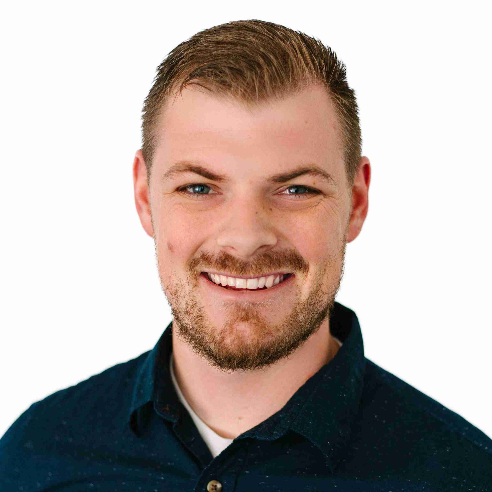 A young man with short light brown hair and a trimmed beard smiles at the camera. Wearing a dark blue collared shirt, he stands against a plain white background—ready to share insights on the Try Invigor podcast.
