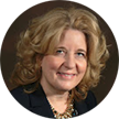 A woman with curly blonde hair is smiling, dressed in a dark-colored blazer and necklace. Set against a plain, dark background, she exudes confidence—perhaps ready to share her secrets to losing weight.