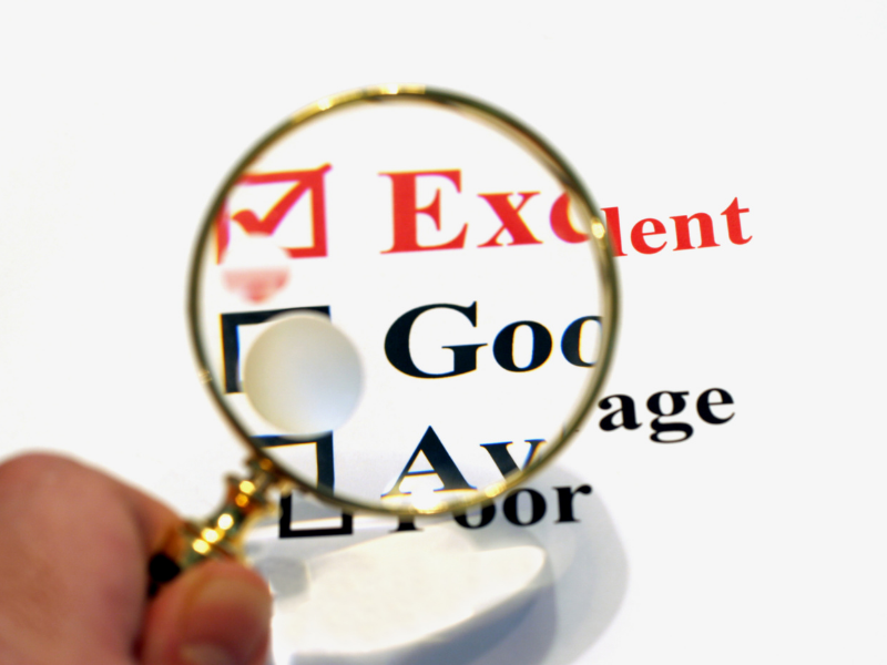 A hand holds a magnifying glass over a checklist, emphasizing a red check mark next to the word Excellent. The other options, Good, Average, and Poor, are not selected and are partially visible.