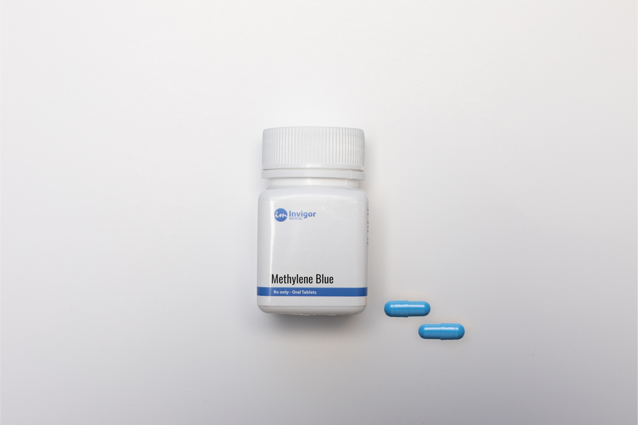 A white bottle labeled Methylene Blue with a white cap sits on a white surface beside two blue capsules—ideal for those looking to Buy Prescription Methylene Blue.