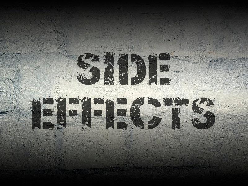 The words SIDE EFFECTS are stenciled in bold, black letters on a textured, light gray concrete wall with a shadowed upper edge.