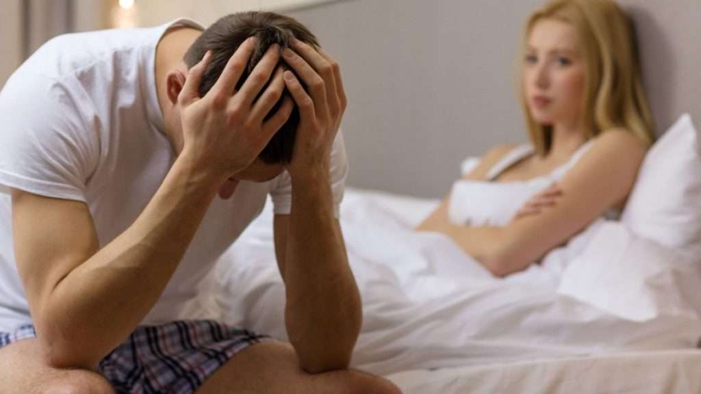 Couple in bed, man sitting with head in hands