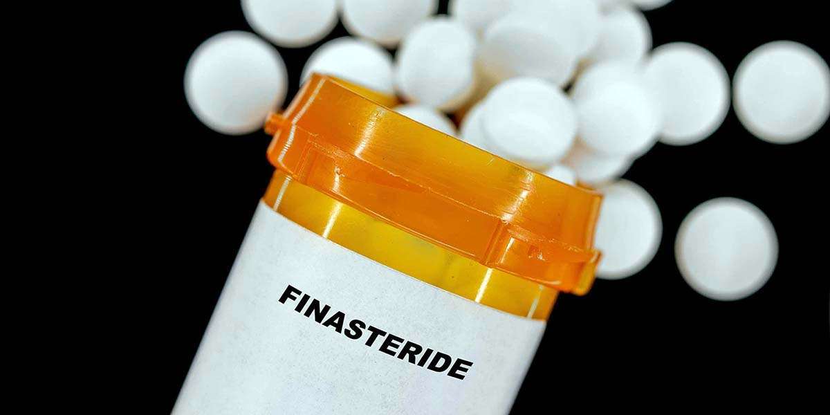A prescription bottle labeled Finasteride lies tipped over, white round pills spilling out against a black background, hinting at questions like how long it takes for Finasteride to work.