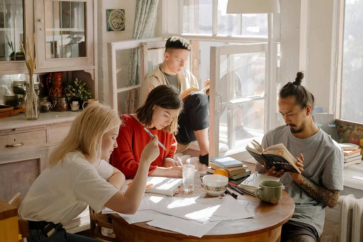 A group of students -- two men and two women -- study around a brightly lit kitchen table with books and papers.